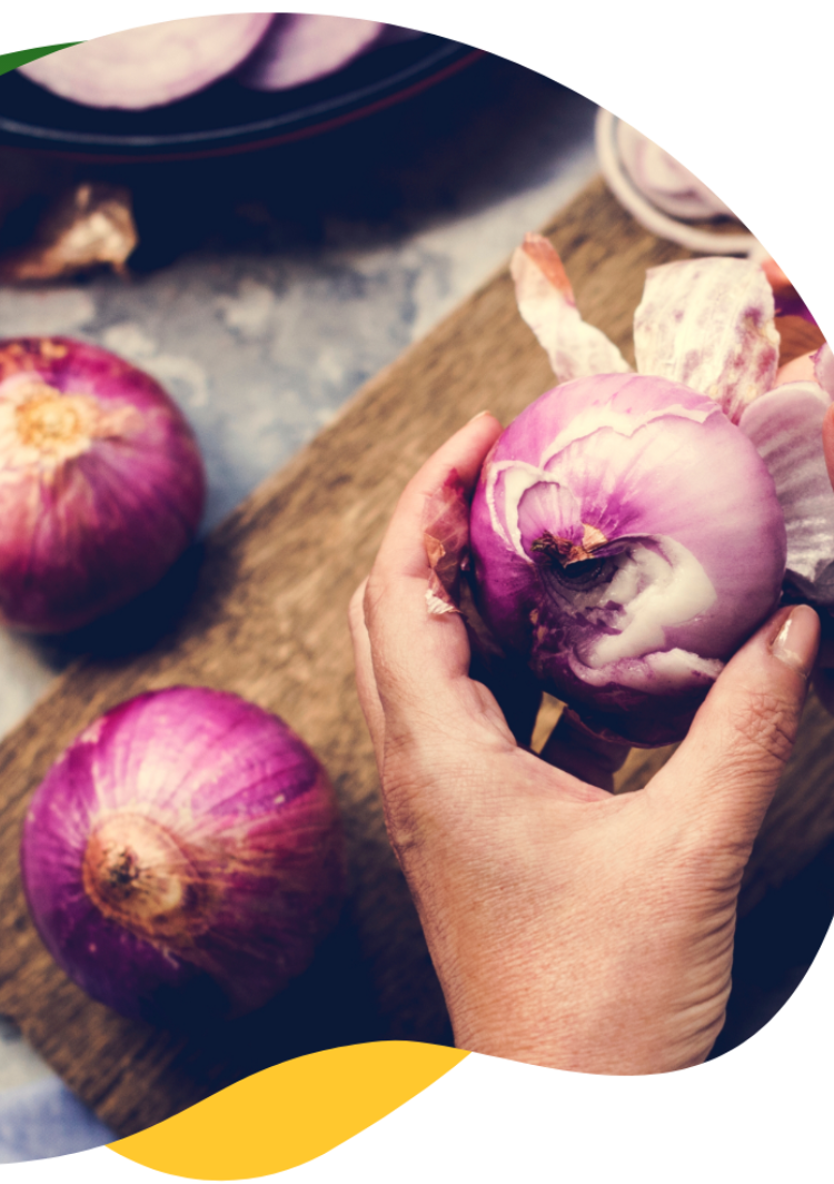 Hands peeling onions on a small board as onions contain fructans which can cause bloating.